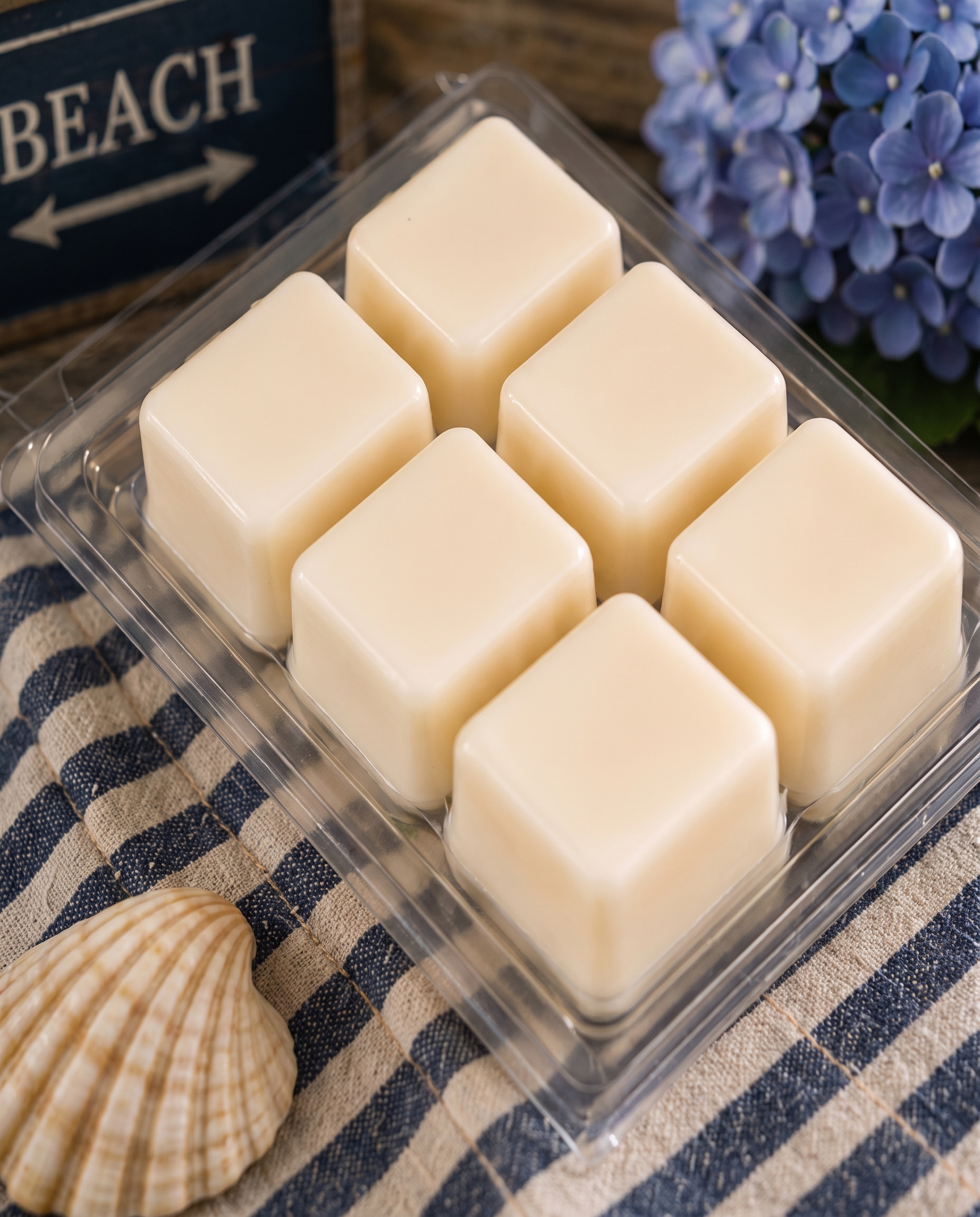 Six cream soy wax cubes in an open Noepe clamshell on a navy striped towel
