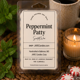 Peppermint Patty wax melts clamshell with mint sprigs and a lit ribbed glass candle