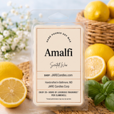 Amalfi scented wax melt clamshell by JARE Candles, surrounded by fresh lemons and basil leaves on a woven rattan mat in bright coastal daylight