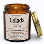 Colada 5oz amber jar candle, lit, lid resting against jar