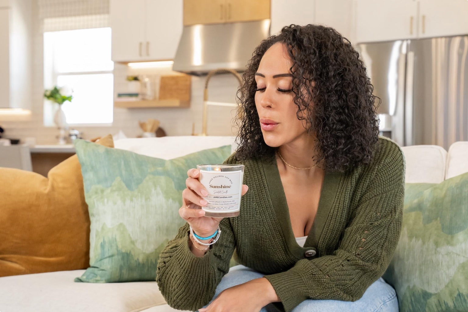 Woman gently blowing out JARE Candles Sunshine soy candle in cozy living room setting