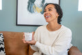 Smiling woman joyfully holding JARE Candles Sunshine candle while seated on leather couch