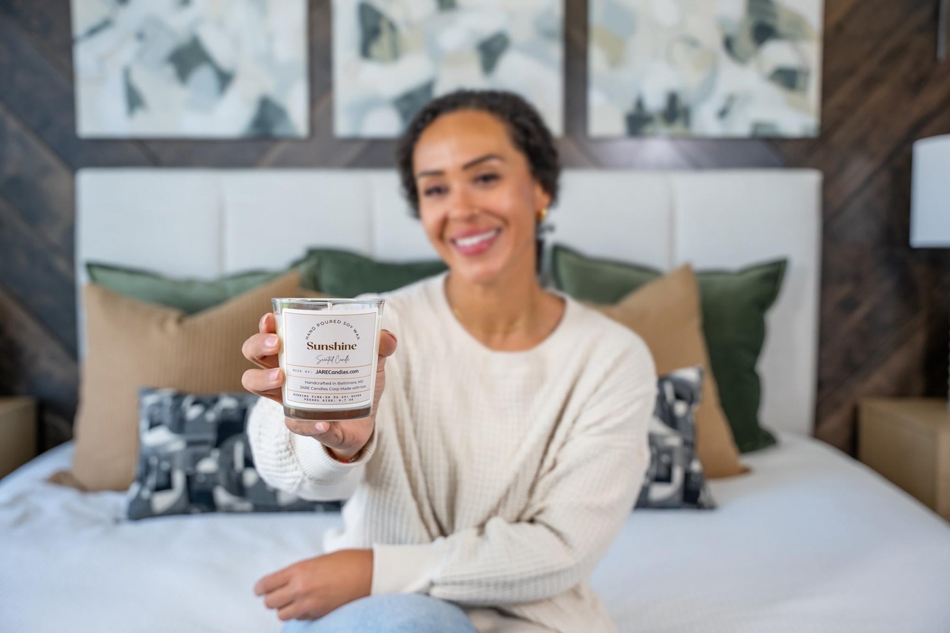 JARE Candles Sunshine soy candle held in focus with smiling woman in soft bedroom setting